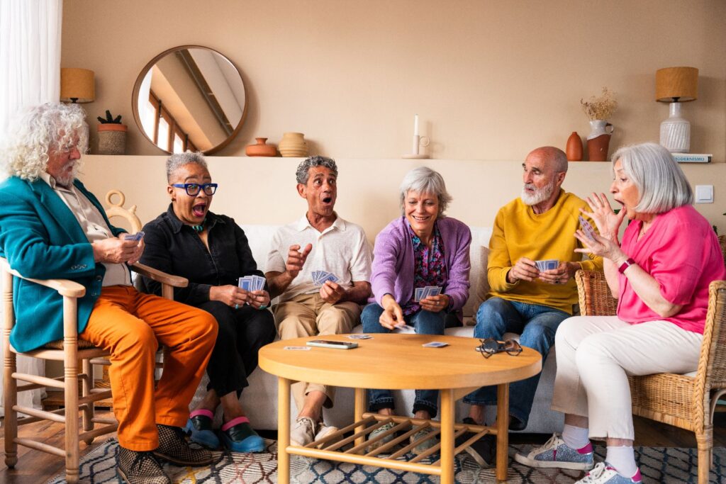 Group of older adults laughing and playing cards together in a cozy lounge — senior living in Brevard.