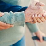 Close-up of a younger person’s hand supporting an older individual’s forearm, with the older person holding a crutch, representing assisted living in Brevard.