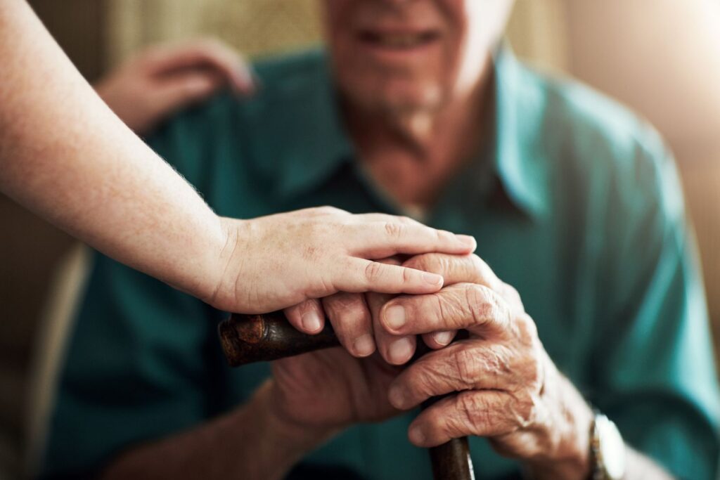 Close-up of a caregiver’s hand resting on an older adult’s hand at College Walk assisted living in Brevard.